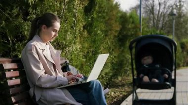Uzaktan kumandalı bir dizüstü bilgisayarda çalışan kadın, yanında bebek arabası, modern iş-yaşam dengesini gösteren kamera, biraz yakınlaştırarak hareket ediyor.