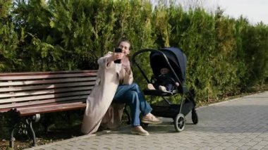 Kadın figürü, akıllı telefonuyla neşeli bir anı yakalıyor, bebek arabasının yanında oturuyor, yeşillikle çevrili, sıcaklığı ve bağlantıyı aktarıyor, kameralar yakınlaşıyor.