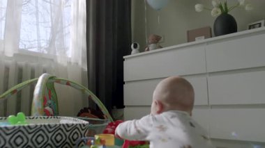 Bebek renkli oyuncaklarla dolu neşeli bir alanı keşfediyor, güneş ışığı sahneyi aydınlatıyor, sıcak ve davetkar bir atmosfer yaratıyor, kamera hareketi takip ediyor