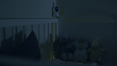 Konforlu oyuncaklar ve bebek monitörüyle rahat bir çocuk odası sahnesi, yumuşak bir şekilde aydınlatılmış, huzurlu bir ortam yaratılmış, kamera huzurlu havayı arttırmak için yavaşça yakınlaşıyor.