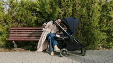 Bej ceketli kadın bakıcı, bir park bankında bebek arabasıyla çarpışır, sıcaklığı ve sevgiyi vurgular, duygusal bağlantı ve sahne ilerlemesini yakalamak için kamera tavaları