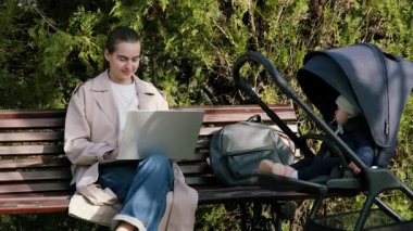 Parktaki bankta otururken bilgisayarla uzaktan kumandalı bir işte çalışan kadın bir bebek arabası, modern iş-yaşam dengesini gösteriyor.