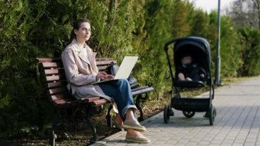 Uzaktan kumandalı bir dizüstü bilgisayarda çalışan, yeşilliklerle çevrili bir bankta oturan, modern iş hayatının dengesini yakalayan serbest çalışan bir kadın.