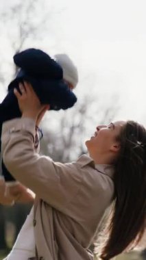 Bir anne çocuğunu havaya kaldırır, neşe ve bağlılık dolu, doğayla çevrili ve atmosferi güzelleştiren nazik güneş ışığıyla dolu hassas bir anı gösterir.