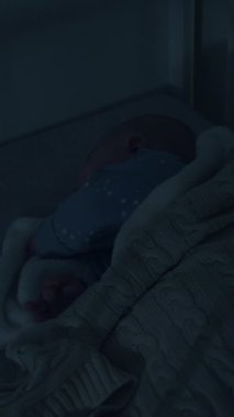 Bebek beşikte huzur içinde uyuyor, yumuşak bir battaniyeye sarılı, loş ışık rahatlatıcı bir atmosfer yaratıyor, kamera sakin sahneyi güzelleştirmek için yavaşça yakınlaşıyor.