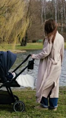 Açık renk ceketli kadın figürü, doğa tarafından çevrelenmiş sakin su kenarında bebek arabasıyla etkileşime girer. Kamera hareketlerini sorunsuz bir şekilde takip ederken huzurlu bir ortam yakalar.