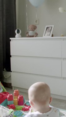 Oyun hasırındaki bebek canlı oyuncaklarla etkileşime girerken, kamera da rahat odayı doğal ışık ve neşe dolu dekorlarla donatıyor.