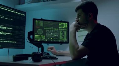 Erkek yapay zeka mühendisi yoğun bir şekilde masasında kodlama yapmakla meşgul. Etrafı verilerle, konsantrasyon ve teknik yeteneklerle dolu parlayan ekranlarla çevrili. Kamera kalıpları ve yakınlaştırmalar.