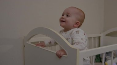 Bebek beşikteki bakıcıyla mutlu bir şekilde etkileşimde, neşeli ifadeler ve şakacı jestler yakalıyor, duygusal bağlantıyı ve sıcaklığı vurguluyor.