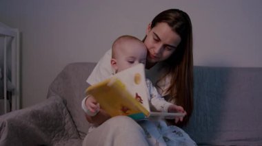 Bir anne bebeğini dingin bir ev ortamında canlı bir hikaye kitabıyla meşgul eder. Bağlarını ve rahatlatıcı atmosferini vurgular. Kamera detaylar için yakınlaşır.