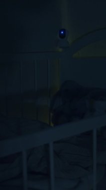 Sıcak çocuk odası sahnesinde battaniyeli bir beşik ve bir izleme cihazı var. Kamera dingin ortama yaklaşırken yumuşak atmosferi yakalıyor.