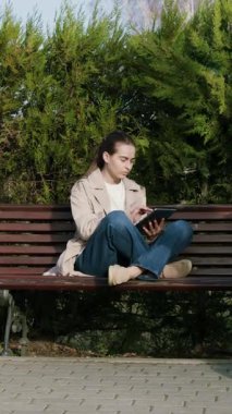 Bir bankta huzurlu bir anın tadını çıkaran bir kadın, yanında bebek arabası olan bir kitap okuyor, yemyeşil bir arazi ile çevrili, sakin atmosferi ortaya çıkarmak için kamera tavaları.