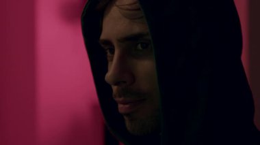 Siyah kapüşonlu erkek hacker yoğun bir odak gösteriyor, pembe ışıkla aydınlatılıyor, siber saldırı sahnesindeki gerilimi ve aciliyeti vurguluyor, kamera dramatik bir etki yaratıyor.