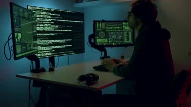 Siber güvenlik analisti birden fazla monitörle derinden ilgileniyor. Kod ve veri gösteriyor, analizin yoğunluğunu gösteriyor, kamera atmosferi yakalamak için yakınlaşıyor.