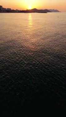 Hava perspektifleri, akşam gökyüzünün sakin atmosferini ortaya çıkaran kameranın zarafetle hareket ettiği canlı günbatımı renklerini yansıtan suyu sergiler.