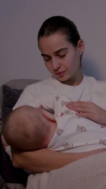 Bir anne bebeğini sevgiyle rahat bir kanepede emzirir. Duygusal bağlantıyı geliştirmek için yumuşak bir zum ile besleyici ilişkiyi ve sıcaklığı ön plana çıkarır.