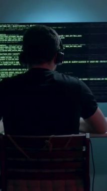 Erkek yapay zeka mühendisi, karmaşık verileri gösteren birçok ekranı olan bir masada çalışmaya dalmış, onun odaklanmasını ve etrafındaki teknolojik çevreyi vurguluyor.