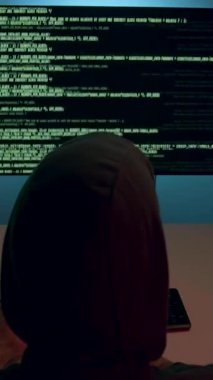 Kapüşonlu şahıs siber saldırıya maruz kalmış, karmaşık kod ve verilerle dolu birden fazla ekranı çalıştırıyor, sahnenin gerilimini ve aciliyetini vurguluyor, kamera yakınlaşıyor