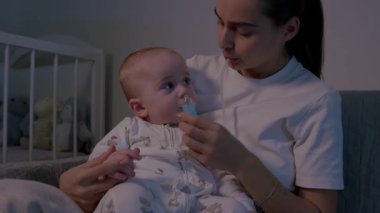 Bir anne bebeğinin burnunu burun aspiratörüyle temizlerken, çocuğun duygusal tepkisini gösteriyor, kamera da mahrem anı yakalamak için yakınlaşıyor.
