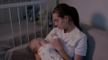 Bir anne, bebeğini yumuşak dokular ve nazik aydınlatmalarla çevrili huzurlu bir kreşte nazikçe emziriyor. Samimi anı vurguluyor. Kamera yavaşça yakınlaşıyor.