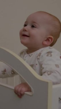 Bebek beşikteki bakıcıyla mutlu bir şekilde etkileşimde, neşeli ifadeler ve şakacı jestler yakalıyor, duygusal bağlantıyı ve sıcaklığı vurguluyor.