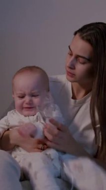 Bir anne evdeki nebulizasyon tedavisi sırasında bebeğini nazikçe rahatlatır, bağ kurma ve yetiştirme atmosferini vurgular, kamera etkileşimlerini ortaya çıkarır.