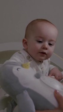 Bebek beşikteki yumuşak bir penguen oyuncağıyla etkileşime giriyor, merak ve neşe sergiliyor, kamera da besleyici çevreyi ve oyuncu anları ortaya çıkarıyor.