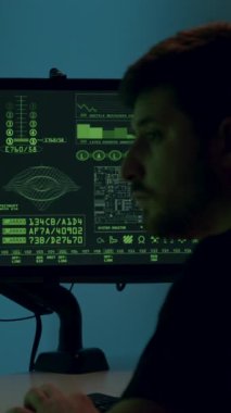 Erkek hacker, siber saldırının atmosferini gösteren kodlarla dolu çift ekran ile derinden ilgilenir. Kameralar onun konsantrasyonunu vurgulamak için yakınlaşır.