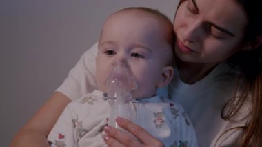 Bir anne sevgi dolu bir şekilde çocuğuna nebulizör tedavisinde yardım eder, sakin ve besleyici bir ortam yaratır, kamera bağlantıyı yakalamak için yavaşça yakınlaşır