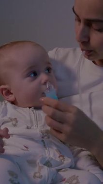 Bir anne bebeğinin burnunu burun aspiratörüyle temizlerken, çocuğun duygusal tepkisini gösteriyor, kamera da mahrem anı yakalamak için yakınlaşıyor.