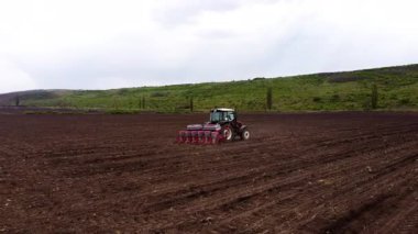 Bir traktör ekme işlemi ile meşgul olur, zengin toprakta izler oluştururken tarımsal teknikler ve mekanizmaları eylem halinde gösterir.
