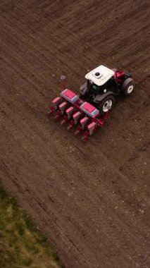 Kırmızı tohumlu bir tarımsal traktör toprağa tohum eker. Bu da ekme sürecini ve modern tarım ekipmanlarının verimliliğini gösterir.