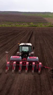 Tohum ekiciyle donatılmış bir tarım traktörü, ekme sürecini ve modern tarım tekniklerinin etkinliğini göstermek için tarla boyunca sürekli hareket eder.
