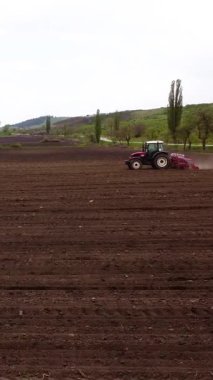 Kırmızı bir traktör kahverengi bir tarlayı sürerek toprak üzerinde görünür çizgiler oluşturur. Toz bulutu yükselirken tarıma hazırlanma sürecini gözler önüne serer.