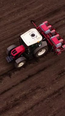 Yerleştirme ekimine sahip kırmızı bir traktör zengin, karanlık topraklarda yol alır, ekme sürecini ve hareket halindeki tarım makinelerini gösterir.