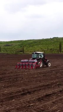 Kırmızı tohum matkabı ile donatılmış bir tarım traktörü toprağı işliyor, tarlada ilerlerken ekim sürecini gösteriyor, gelecekteki ekinlere hazırlanıyor.