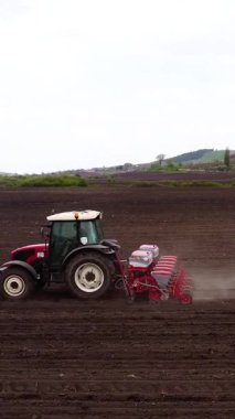 Kırmızı bir traktör tohum matkabını çalıştırıyor, yeni dönüştürülmüş toprağa tohum ekiyor, tarımsal uygulamaları ve mekanizmaları iş başında gösteriyor.