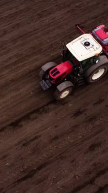 Kırmızı bir traktör toprak hazırlamakla uğraşır, onu yakından takip eden tohum tatbikatı tarımsal bir ortamda sürme ve dikme eylemlerini gösterir.