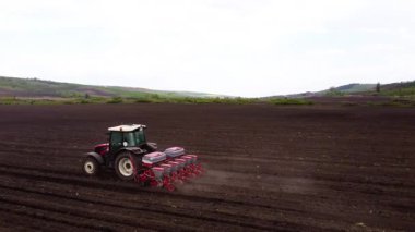 Bir traktör geniş bir tarlaya tohum ekmeye çalışır. Toprak rahatsız edilirken tarımsal teknikler ve sürekli hareket halinde olan makineler gösterir.