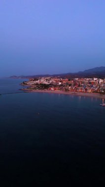 Hava perspektifi alacakaranlıkta çarpıcı bir kıyı şeridini gözler önüne seriyor, su üzerinde canlı yansımalarla, kamera pürüzsüz bir şekilde yansıyor, sakin atmosferi ve resimsel manzarayı vurguluyor