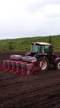 Tohum bitkileriyle donatılmış bir tarım traktörü tohum tohumlarını yeni sürülmüş toprağa yerleştiriyor. Bu da açık bir alanda ekme ve toprak etkileşimini gösteriyor.