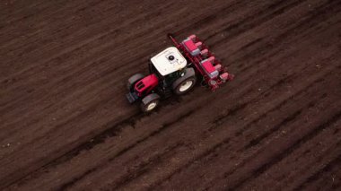 Tohum matkabı ile donatılmış kırmızı bir traktör, toprak hazırlama ve ekme faaliyetleriyle uğraşarak tarımsal verimliliği ve mekanizmayı iş başında göstererek, sürekli olarak tarlada hareket eder.