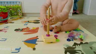 Genç bir çocuk ahşap bir askıya renkli yüzükler yığar, oyuncaklarla dolu canlı bir oyun odasında motor becerilerini ve konsantrasyonunu gösterir.