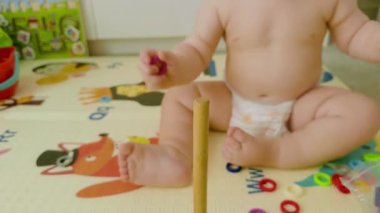 Genç bir çocuk dikey tahta bir direğin üzerine renkli yüzükler yığmaya odaklanır, güzel motor becerileri sergiler ve yumuşak, resimli bir oyun paspası üzerinde eğlenceli keşifler yapar.