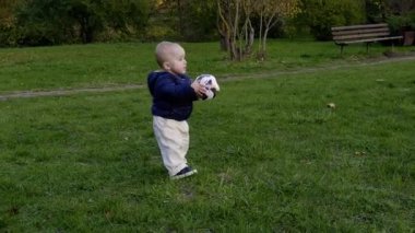 Mavi ceketli bir çocuk çimenli arazide bir futbol topuyla karşılaşır, dışarıdaki çevreyi incelerken merak ve hareket gösterir.