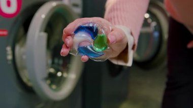 Çamaşır deterjanı kapsüllü bir kadın, çamaşır makinesindeki çamaşır makinesine beyaz yatak koymaya hazırlanıyor.