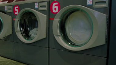 Çamaşırhanedeki çamaşır makineleri sürekli yüklenen çamaşırları görünür döngüler ve açık cam kapılarla gösteriyor.