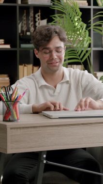 Bir masadaki öğrenci dizüstü bilgisayarla meşgul oluyor, kitaplıklar ve bitkilerle sıcak bir çalışma ortamı yaratıyor.