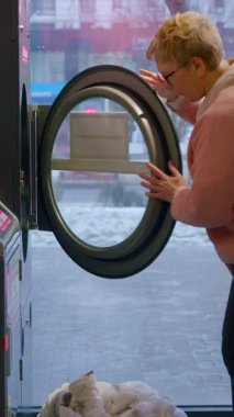 Beyaz kadın çamaşırları çamaşır makinesine yerleştirir ve kontrol panelinin ayarlarını parlak, modern çamaşırhanenin iç kısımlarına ayarlar.