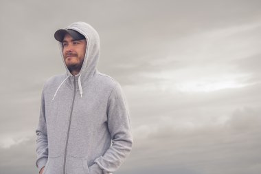 Kapüşonlu ve bulutlu bir günde ile beysbol şapkası giyen genç adam 